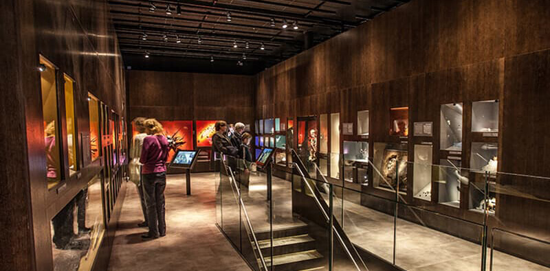 Mørkt rum med udstilling og turister indenfor i Moesgaard Museum